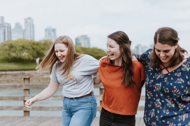 Three women walking with their arms around each other laughing
