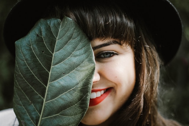 Girl smiling half her face hidden behind a big green leaf